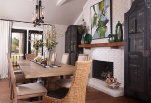 Long rectangular dining room table next to a white brick fire place with artwork and accessories